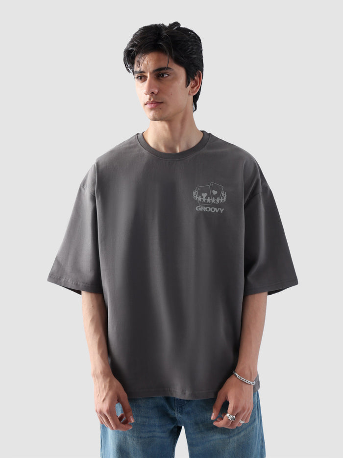 Male model wearing stone grey oversized t-shirt in Pakistan by Groovy – drop shoulder, baggy fit graphic tee styled with loose denim jeans
