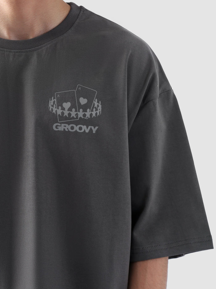 Male model wearing stone grey oversized t-shirt in Pakistan by Groovy – drop shoulder, baggy fit graphic tee styled with loose denim jeans