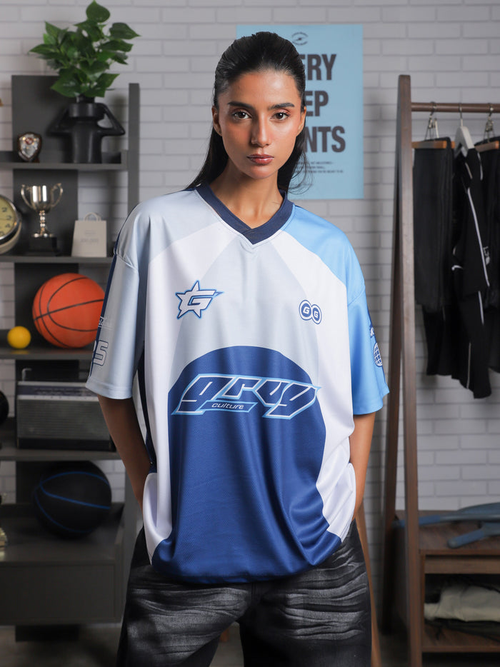 Woman wearing oversized blue and white racing jersey with bold graphics – Groovy Culture unisex streetwear shot in lifestyle indoor setup Pakistan